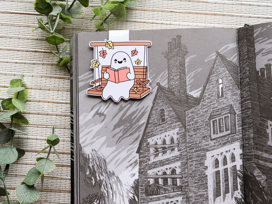 Magnetic bookmark featuring cute ghost smiling while reading on a swing with some orange and yellow leaves falling